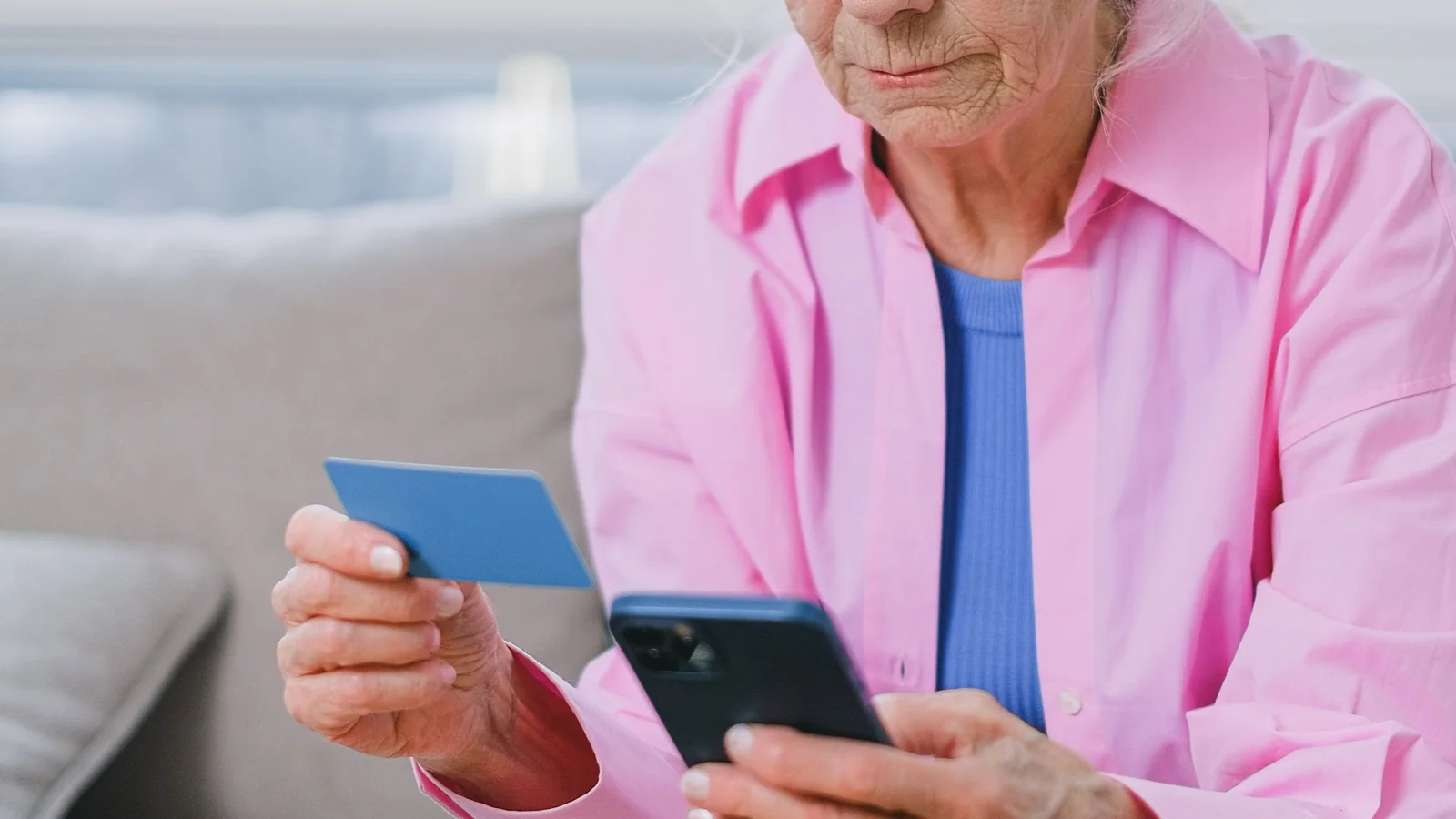 Une femme âgée tient une carte bancaire et consulte son smartphone à son domicile