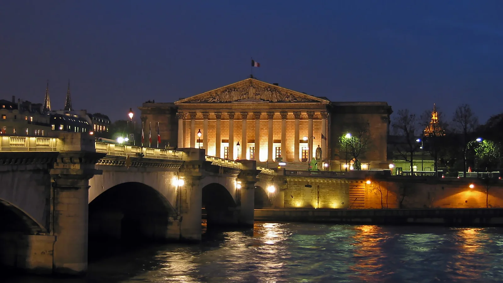 Façade éclairée du Palais Bourbon, siège de l’Assemblée nationale, vue de nuit depuis la Seine