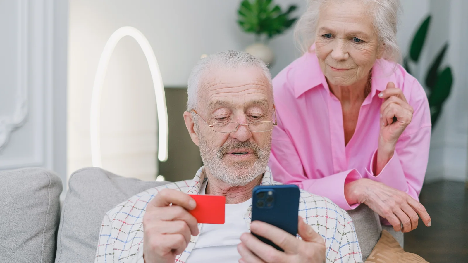 Un couple de seniors consulte un smartphone avec une carte bancaire à la main