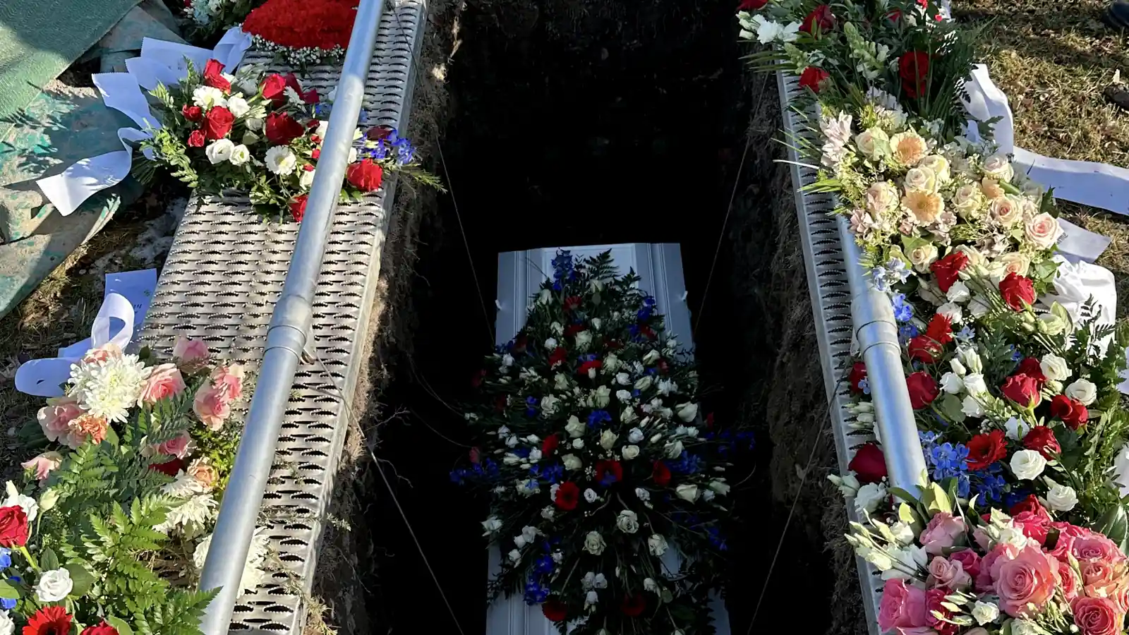Cercueil blanc entouré de gerbes de fleurs dans une tombe ouverte