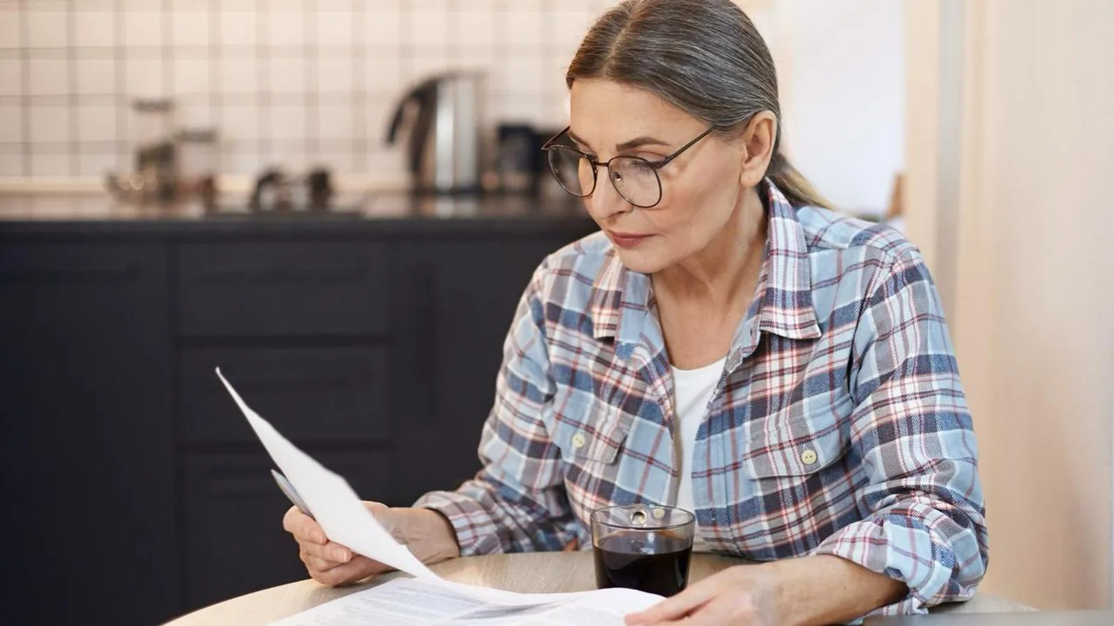 Une femme consulte des documents financiers à sa table, pour illustrer la préparation d'une donation familiale