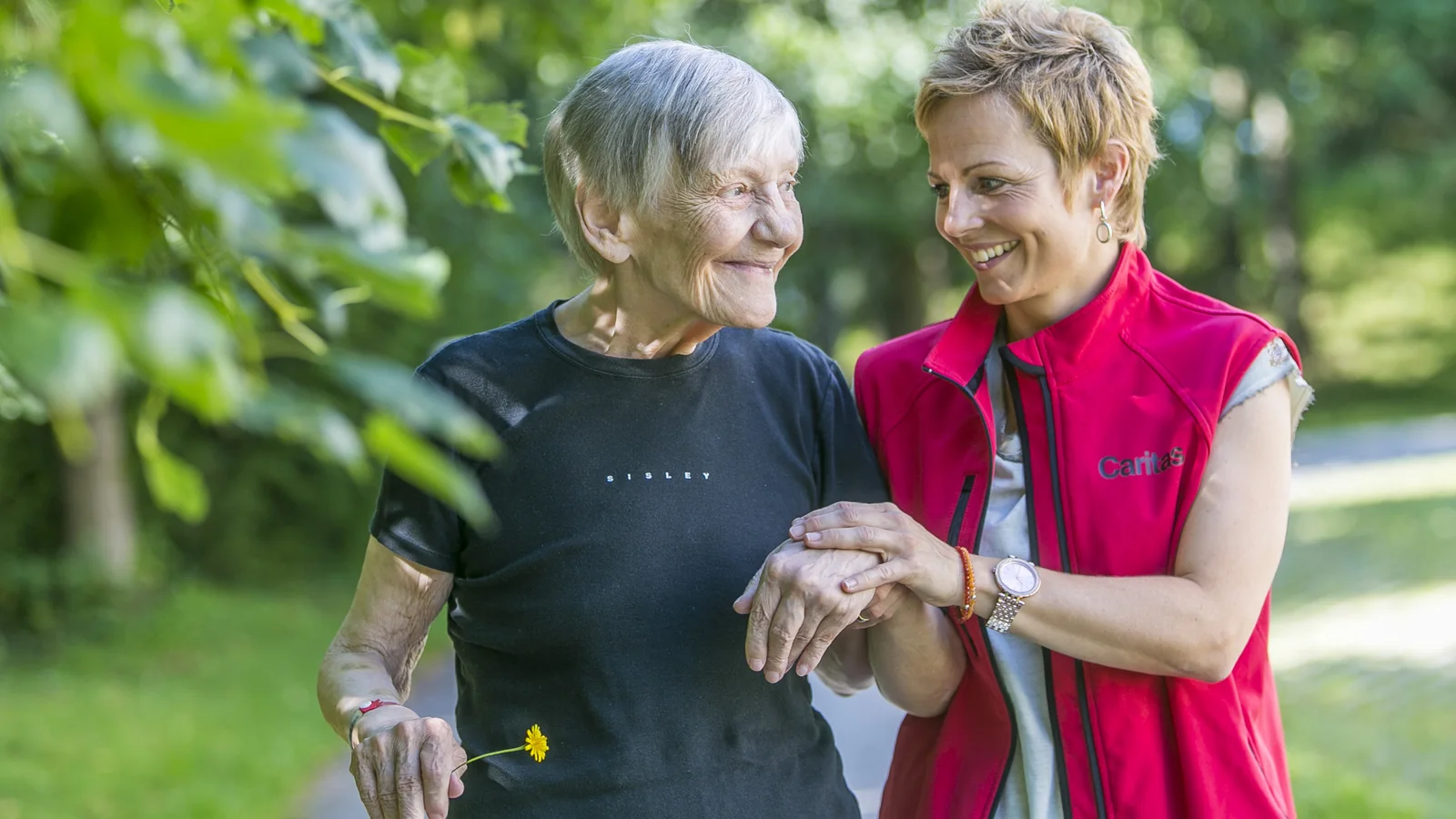 Une professionnelle de l’accompagnement soutient une femme âgée lors d’une promenade