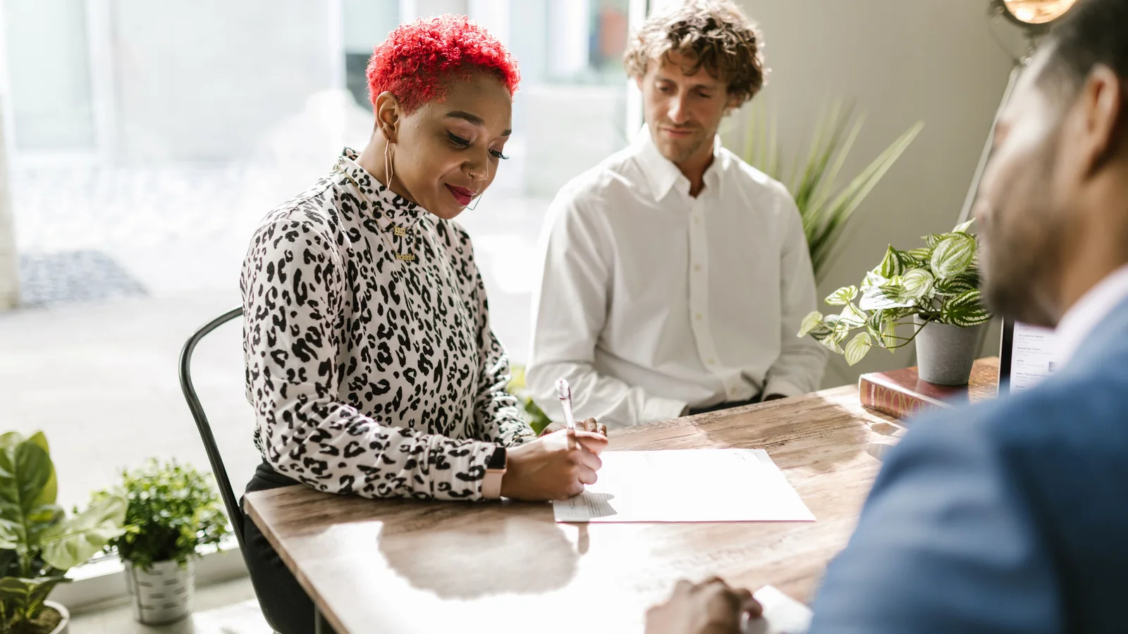 Une femme signe des documents face à 2 conseillers dans un bureau